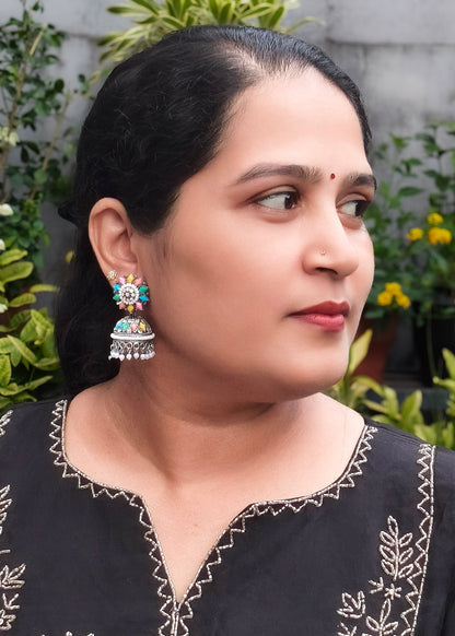 A woman wearing a colorful, ornate silver-toned jhumka earring.