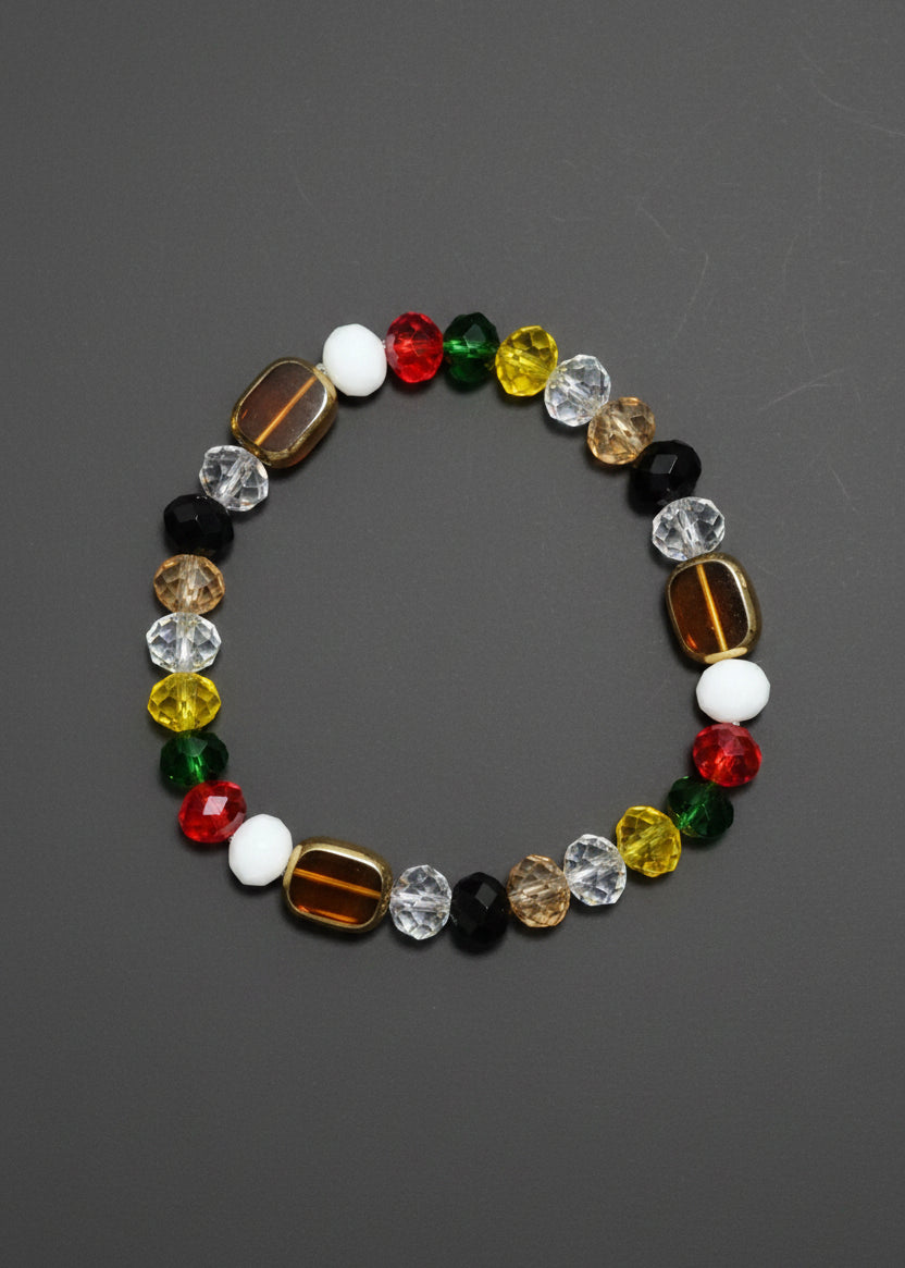 A beaded stretch Navagraha bracelet featuring a mix of colorful faceted beads in red, green, yellow, white, black, and metallic gold, arranged in a circular shape on a textured blue background.