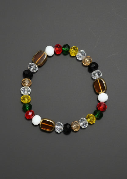 A beaded stretch Navagraha bracelet featuring a mix of colorful faceted beads in red, green, yellow, white, black, and metallic gold, arranged in a circular shape on a textured blue background.