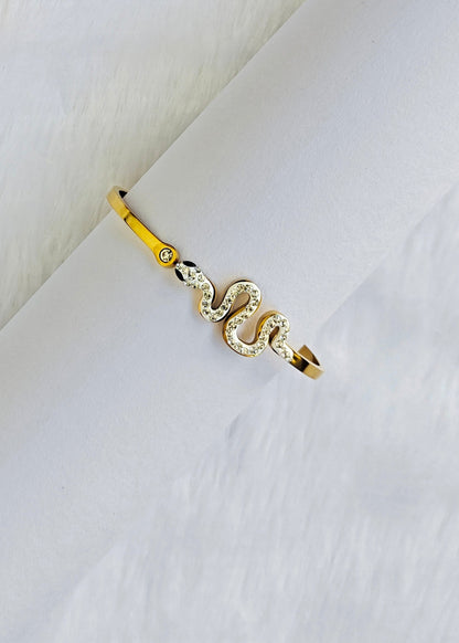 A gold snake ring with clear crystal accents, displayed on a white textured surface.