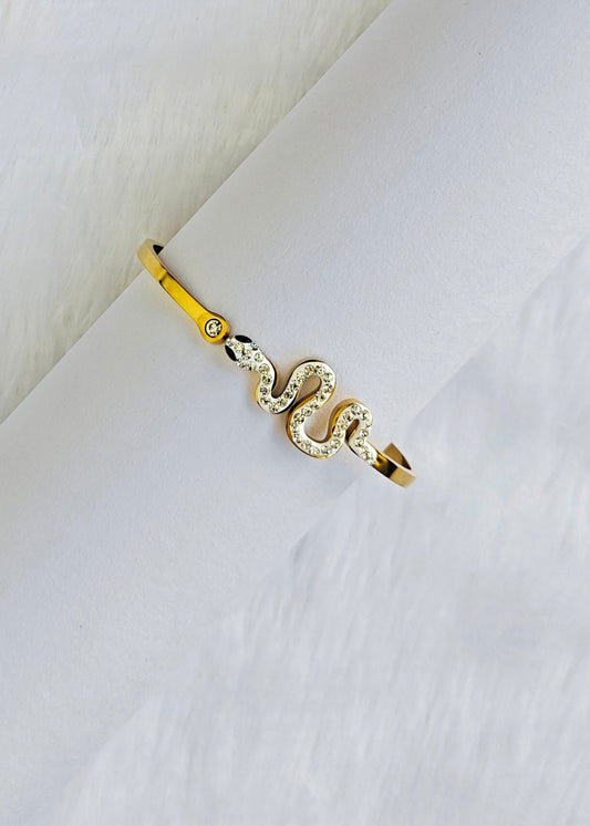 A gold snake ring with clear crystal accents, displayed on a white textured surface.