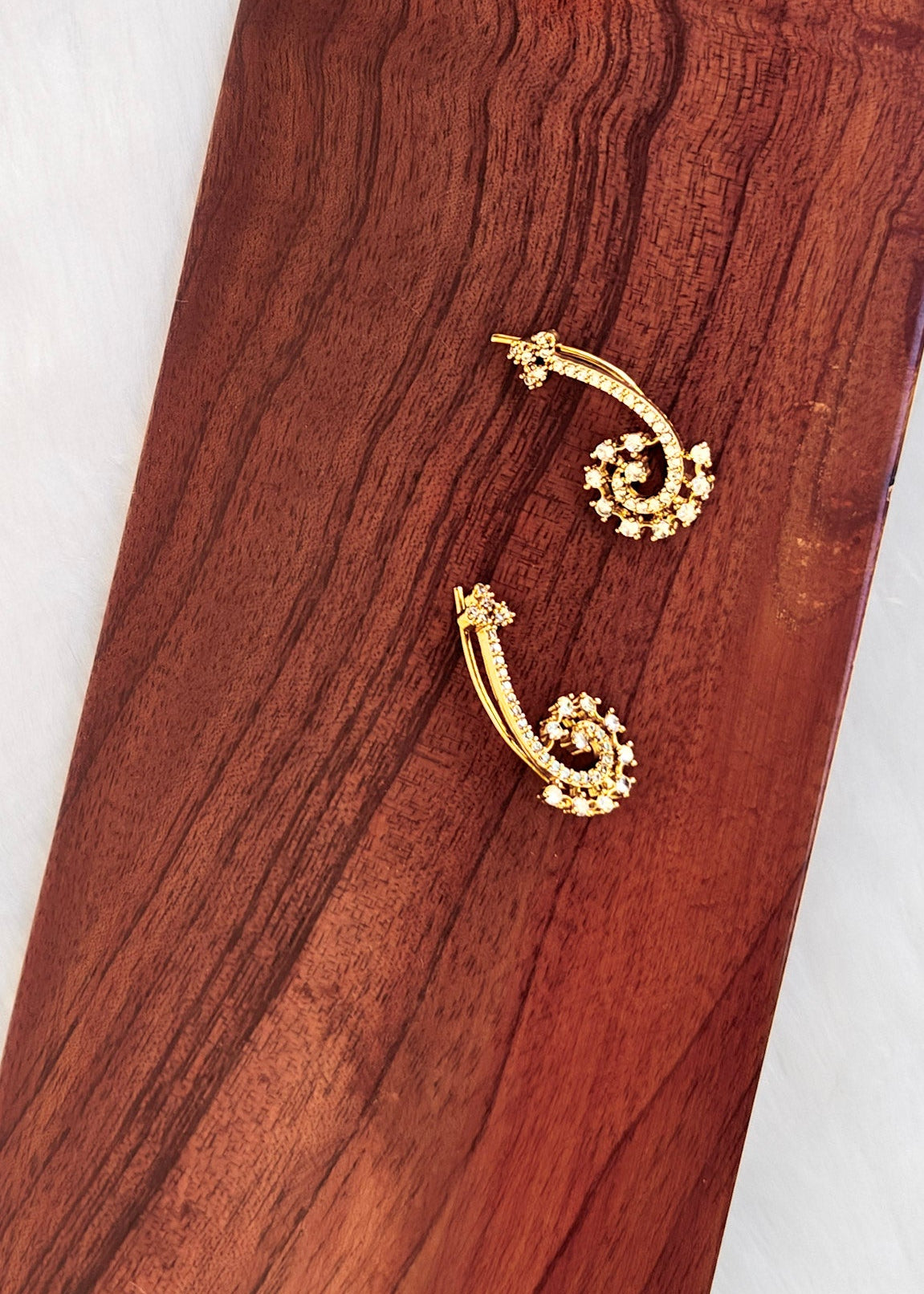 A pair of gold-toned huggie hoop earrings with floral details.