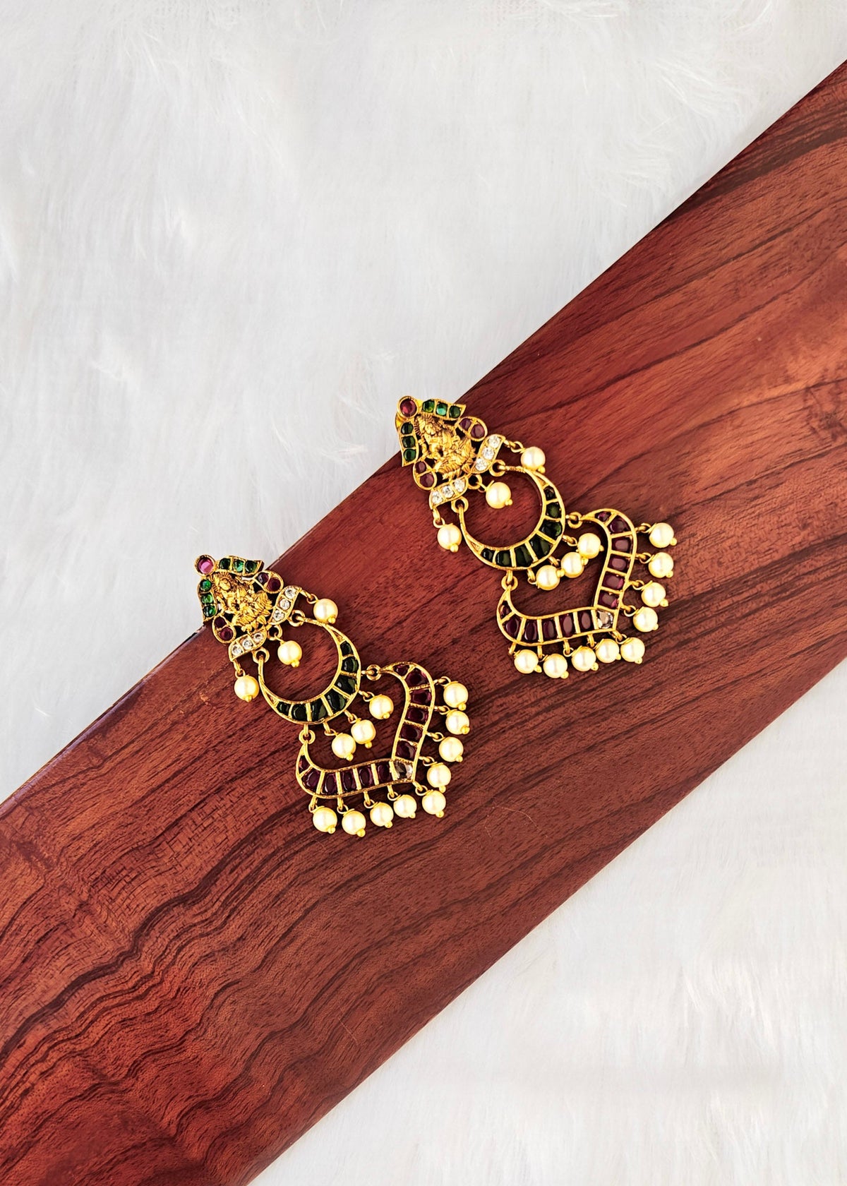 A pair of gold-toned traditional Indian jhumka earrings with green and red enamel detailing and white bead fringe.
