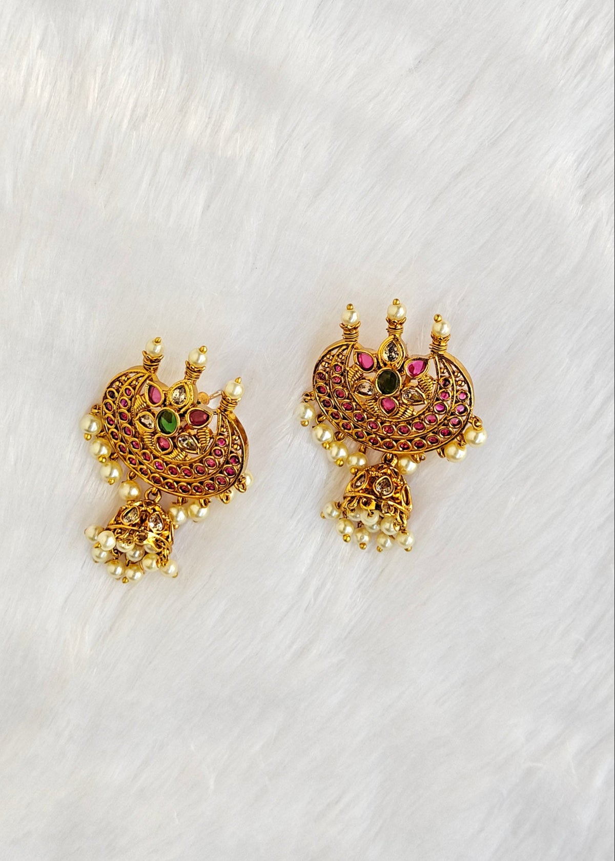 A pair of ornate gold-toned traditional earrings with intricate filigree work, small pearl-like bead accents, and red and green stone details.