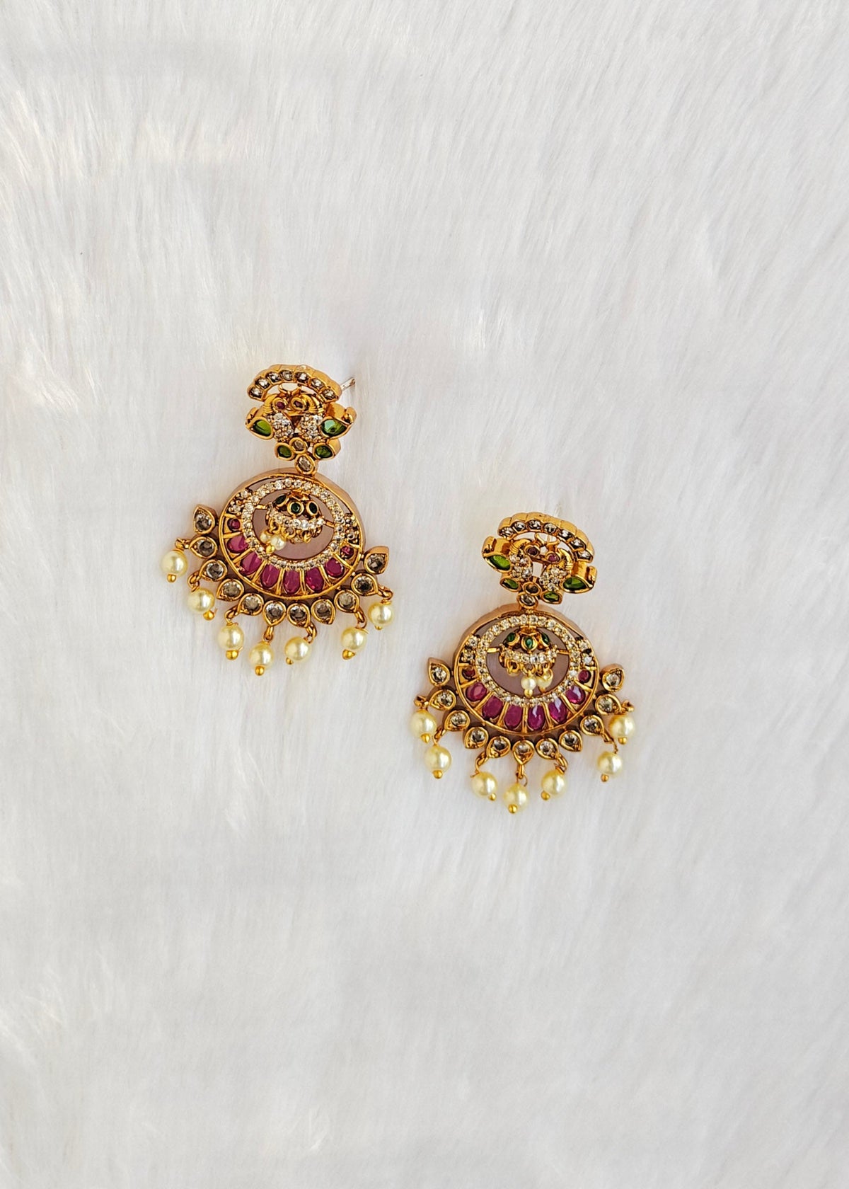 A pair of ornate gold-toned Indian jhumka earrings decorated with red and green enamel, featuring dangling pearl-like beads.