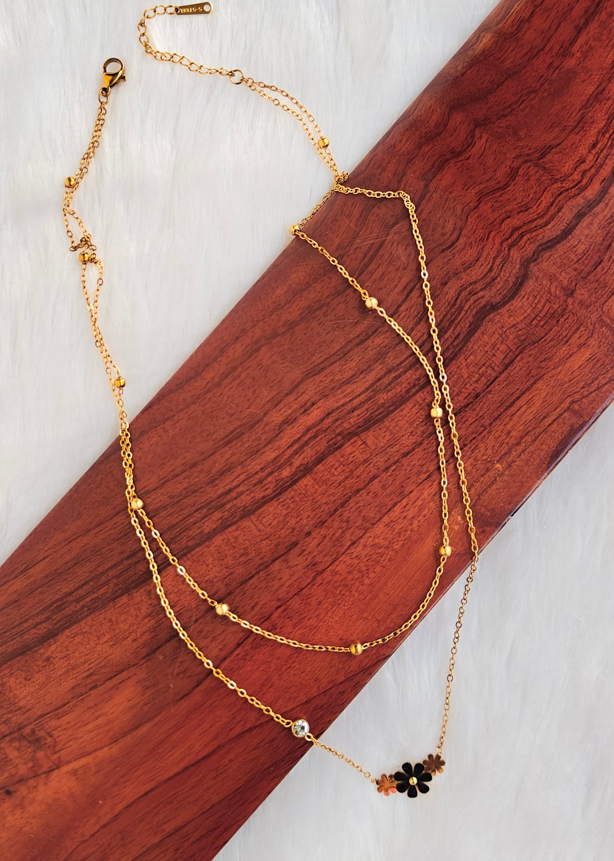 A gold double-strand anti tarnish necklace with a small floral charm featuring black and brown petals, 