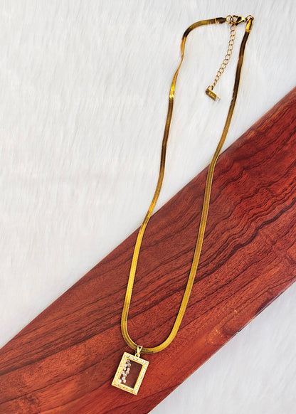 A gold-toned snake chain necklace with a rectangular pendant featuring a small portrait engraving, 