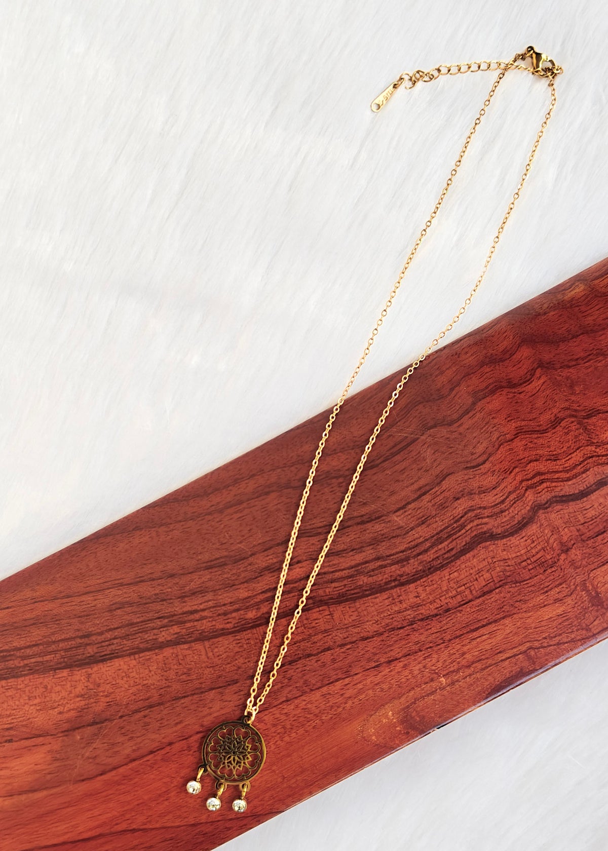 A gold-toned chain necklace with a round medallion pendant and three small dangling pearl-like beads, 