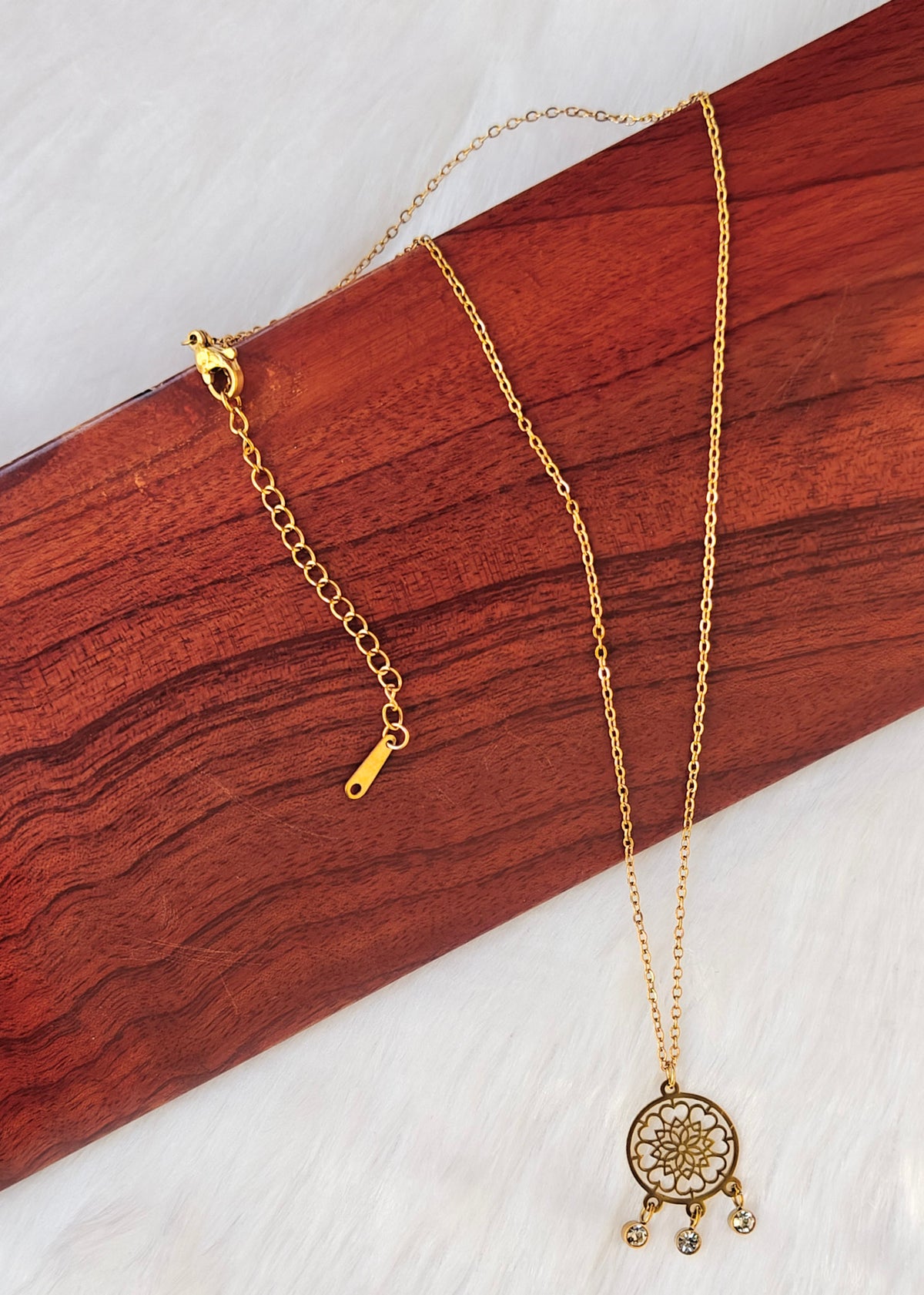 A gold-toned necklace with a circular mandala pendant and small dangling charms,