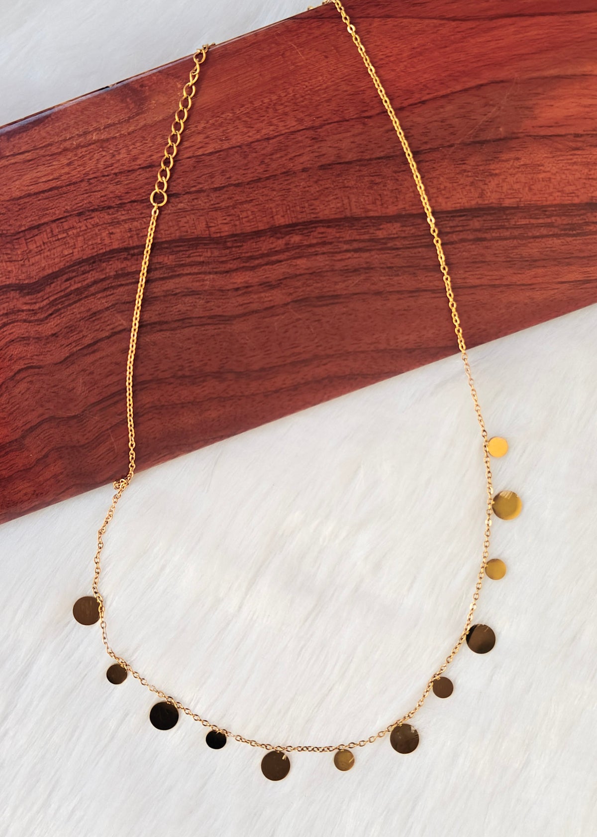 A delicate gold chain necklace with multiple small, flat circular disc charms in varying metallic gold and bronze finishes