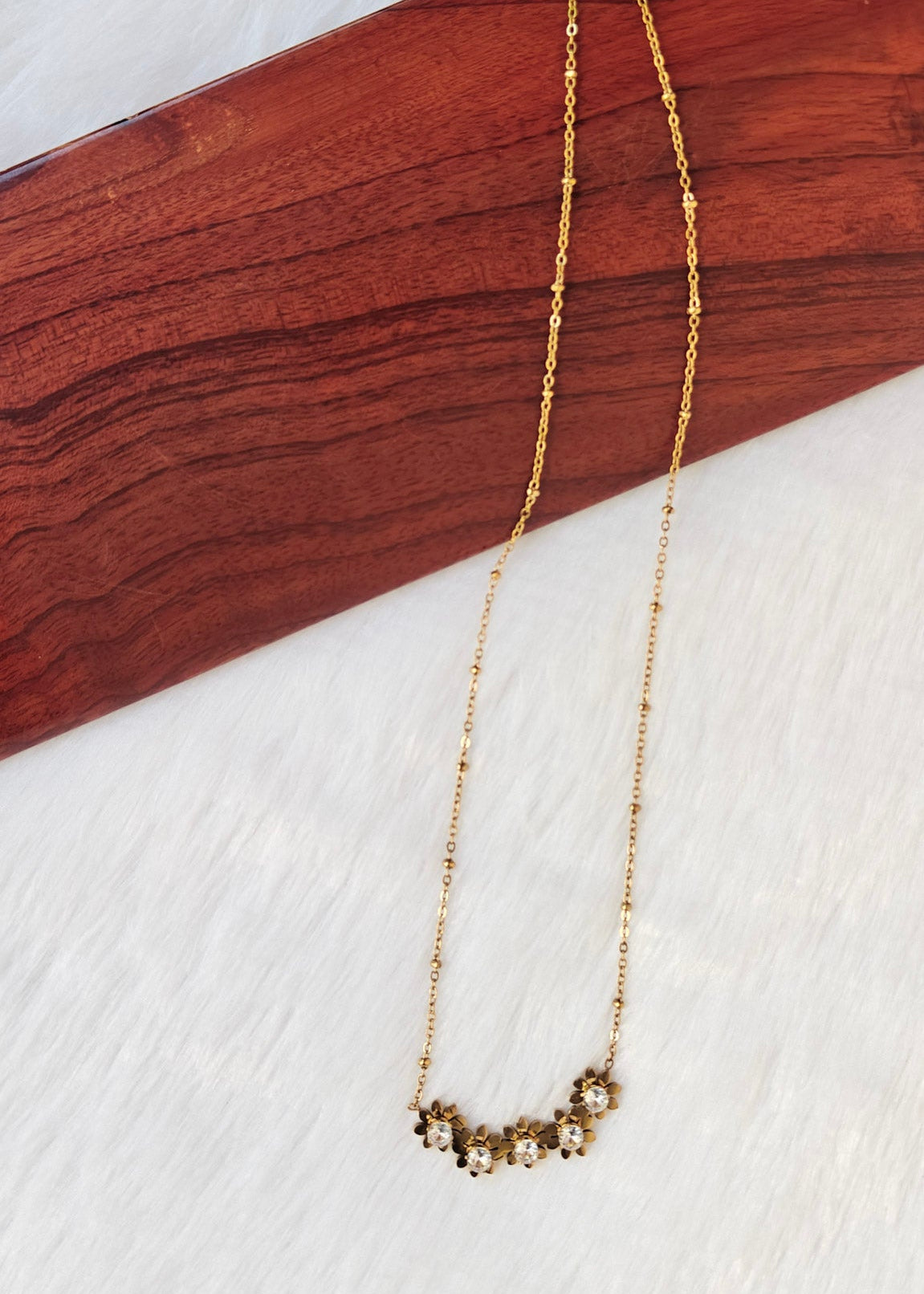 Jenny floral rhinestone necklace laid on cream fabric, showing the gold-toned beaded chain and extension clasp.