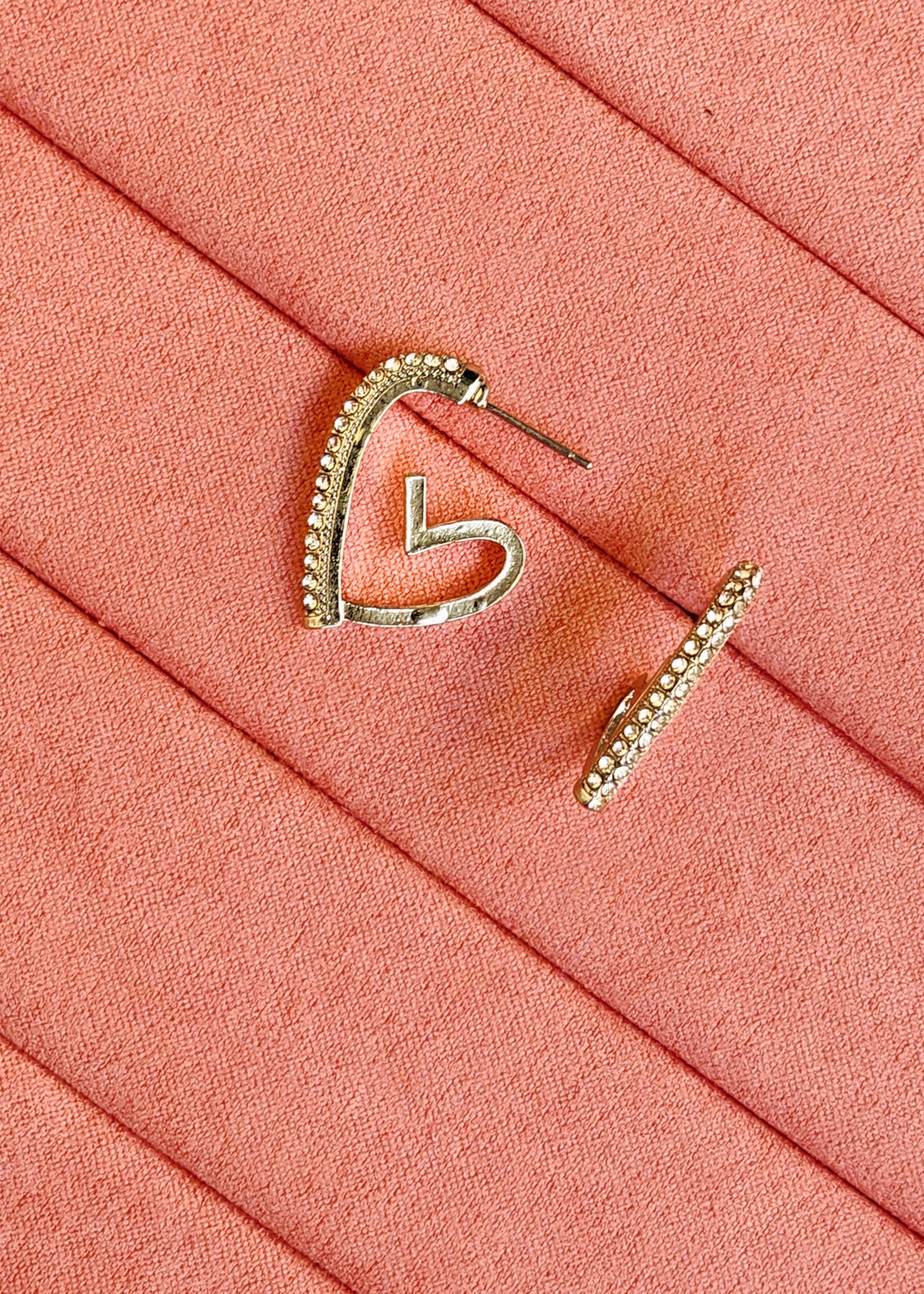 A pair of silver-toned hoop earrings with small clear stones along the top curve, displayed on a textured coral-pink surface.