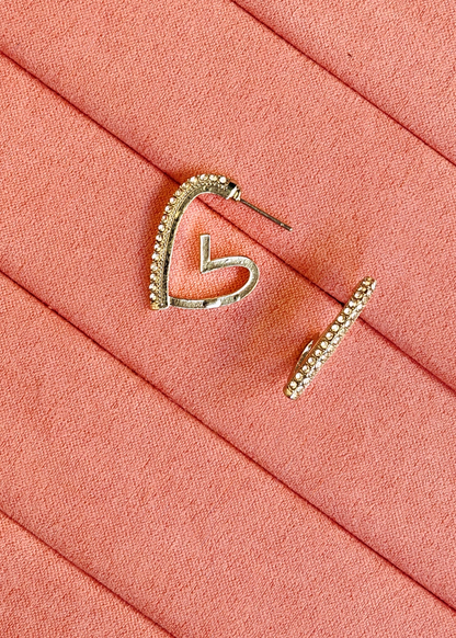 A pair of silver-toned hoop earrings with small clear stones along the top curve, displayed on a textured coral-pink surface.