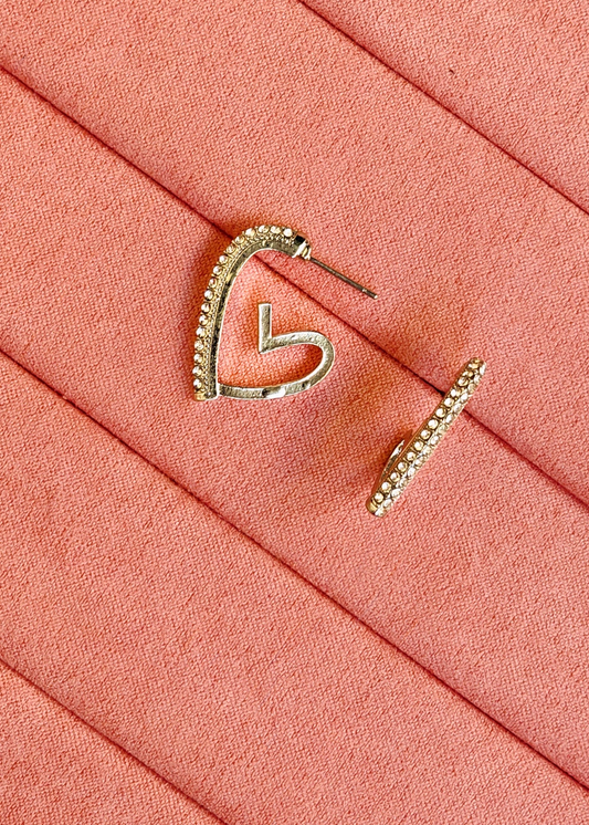 A pair of silver-toned hoop earrings with small clear stones along the top curve, displayed on a textured coral-pink surface.