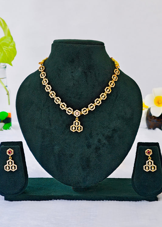 Gold-toned jewelry set displayed on a black velvet mannequin bust, including a necklace with a central pendant and matching drop earrings, shown against a light background with small decorative flowers.