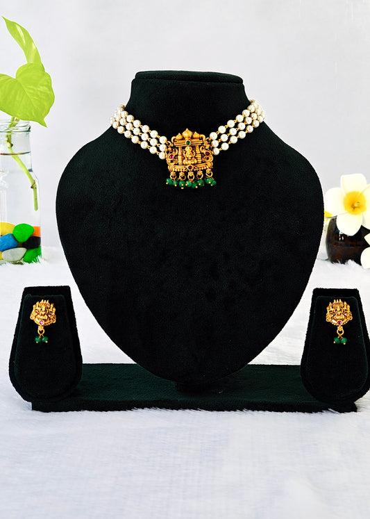 A gold and green jewelry set displayed on a black velvet mannequin bust, including a pearl-beaded necklace with a central ornate gold pendant, matching drop earrings, and small standees, set against a white background with decorative flowers.