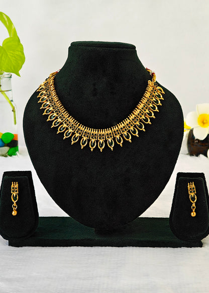 Gold-toned traditional Indian jewelry set featuring a choker necklace, matching drop earrings, and a matching ring, displayed on a black velvet jewelry bust and stand against a white background with decorative flowers.