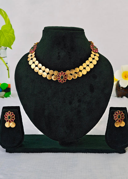 Gold coin necklace and matching earrings displayed on a black velvet jewelry bust set against a light gray background with decorative green and white flowers.