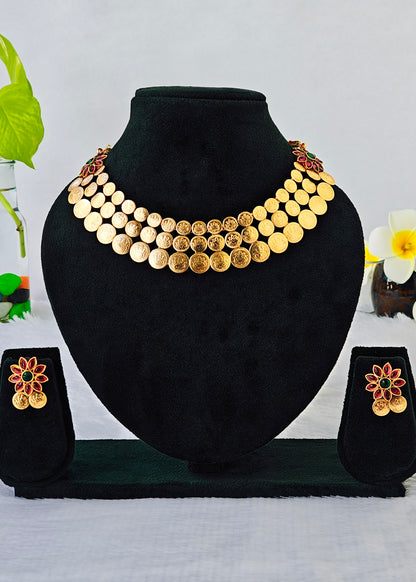 A gold coin necklace set displayed on a black velvet jewelry bust, with matching flower-shaped earrings on small display stands. The necklace features multiple rows of round gold coins with some engraved details, and the earrings have gold coin details with red and green enamel accents.
