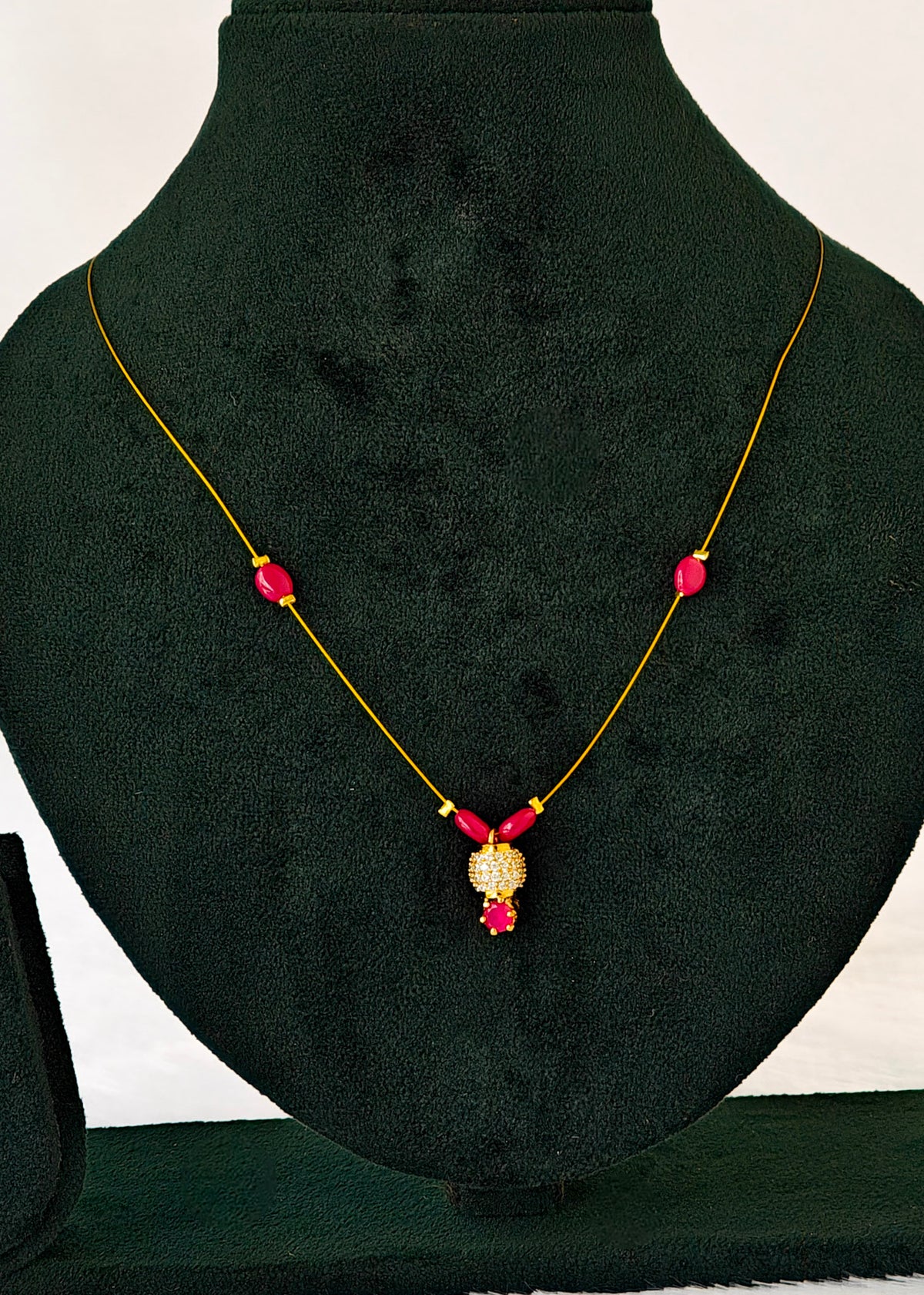 A gold necklace with three pink gemstone beads and a central gold pendant with pink stones, displayed on a black velvet jewelry bust.