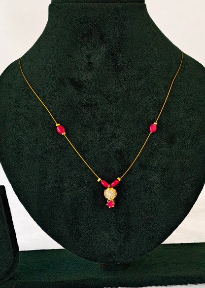 A gold necklace with three pink gemstone beads and a central gold pendant with pink stones, displayed on a black velvet jewelry bust.