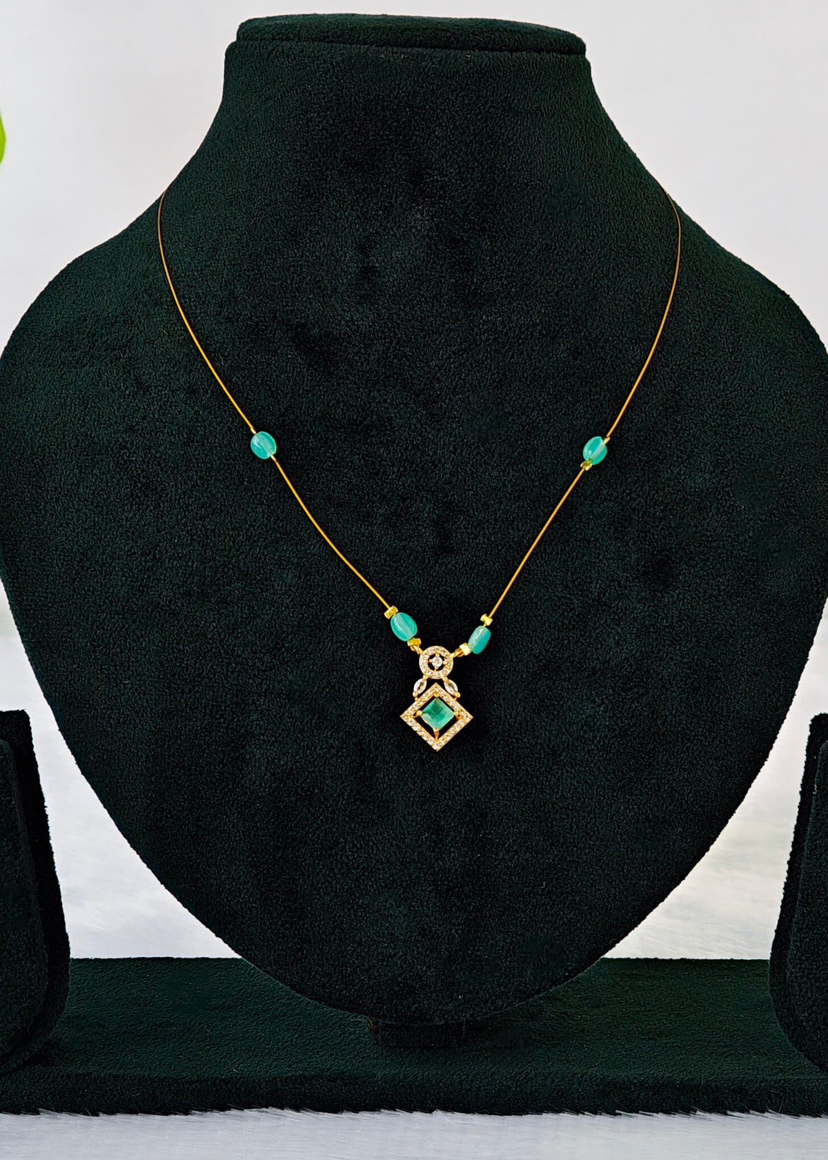 A gold necklace with turquoise-colored beads and a geometric pendant, displayed on a black velvet jewelry bust.