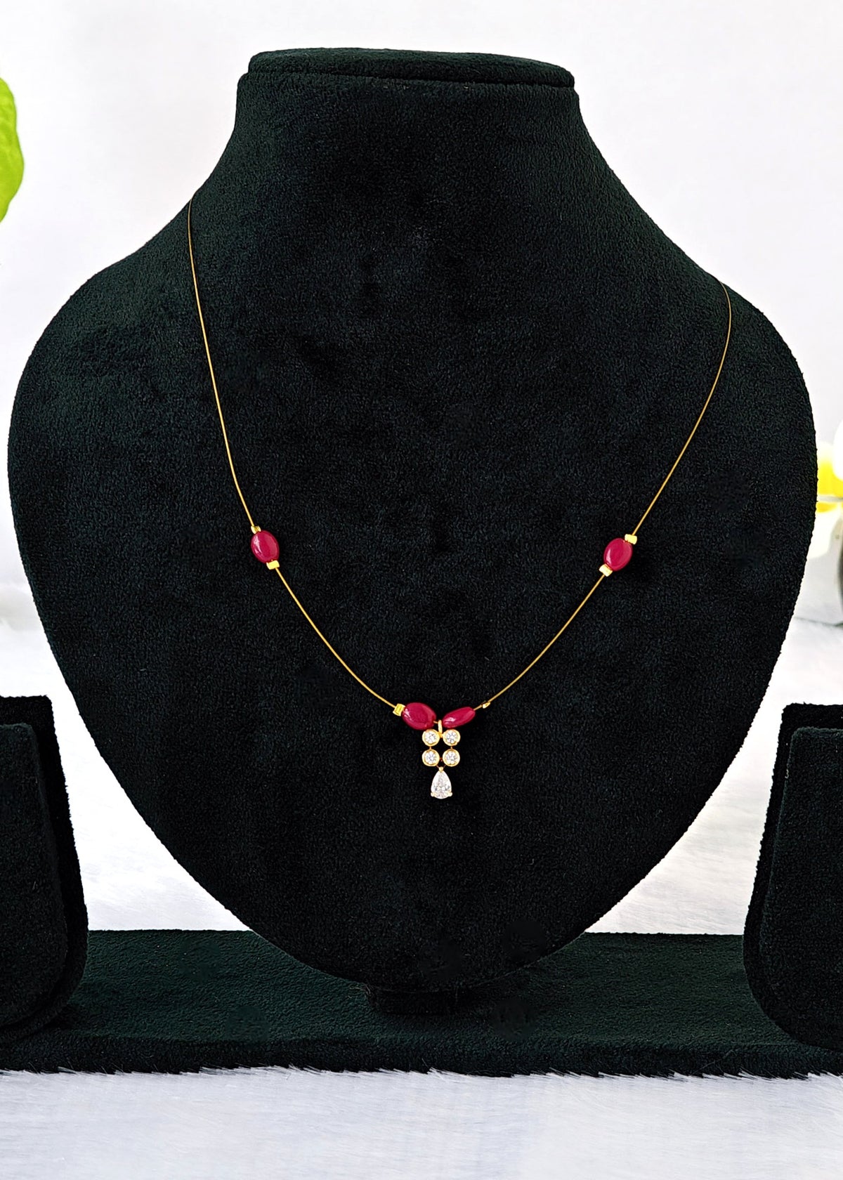 Kashish fine-wire necklace with ruby-red oval beads, a white crystal cluster and teardrop pendant on a black display.