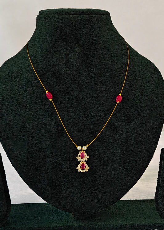 A gold necklace with red and white gemstone accents displayed on a black velvet jewelry bust.