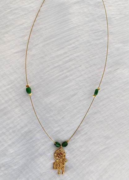 A delicate gold chain necklace featuring a small gold monkey pendant and two green oval beads spaced along the chain, displayed on a textured white fabric background.