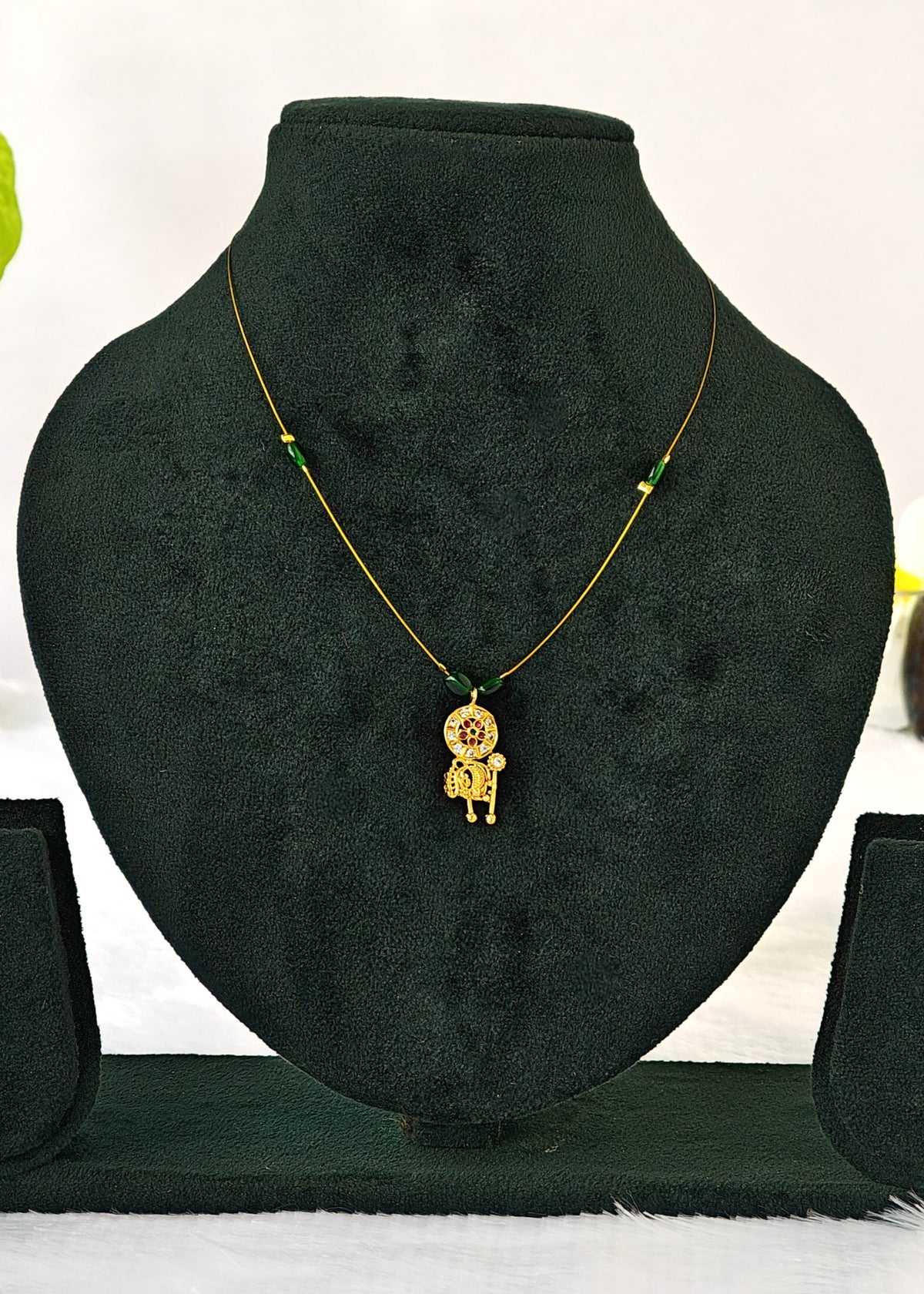 Avani fine-wire necklace with green beads and a floral mandala and elephant pendant on a black display.
