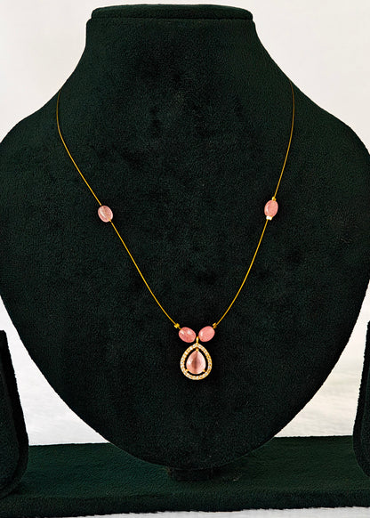 A delicate gold chain necklace with pink gemstone accents, displayed on a black velvet jewelry bust. The necklace features a central teardrop-shaped pink gemstone surrounded by a small gold border, with smaller pink gemstones spaced along the chain.
