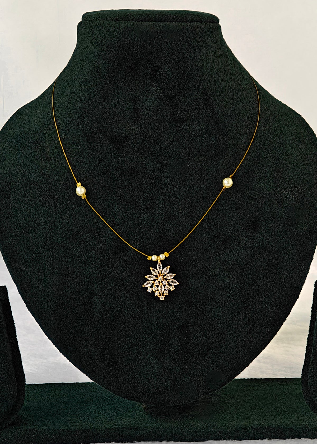 A delicate gold necklace with a central gold snowflake pendant and small gold beads, displayed on a black velvet jewelry bust.