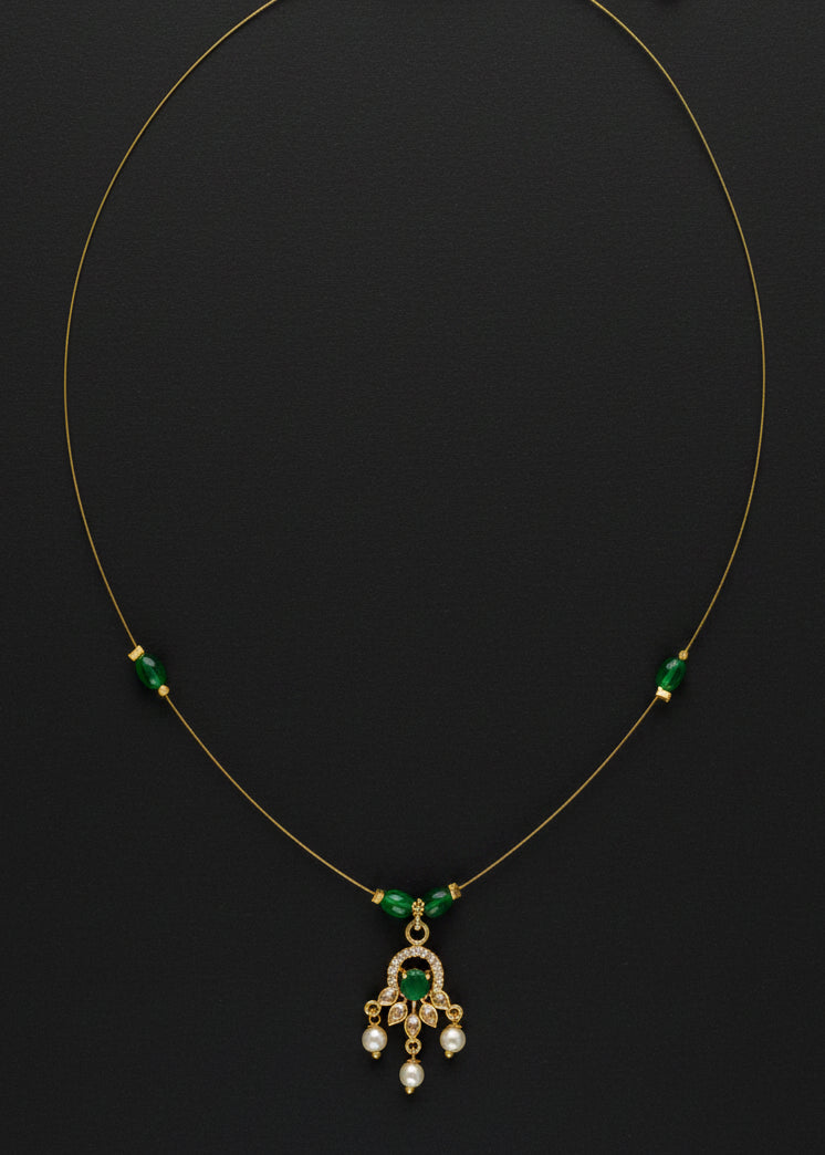 A delicate gold chain necklace featuring three small green bead accents on either side of a central gold pendant with green and clear stones