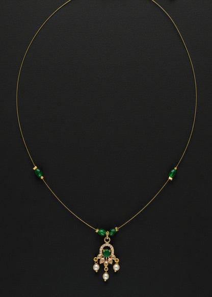 A delicate gold chain necklace featuring three small green bead accents on either side of a central gold pendant with green and clear stones