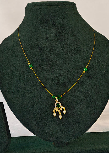 A gold chain necklace with green bead accents and a dangling pendant, displayed on a dark green velvet jewelry bust.