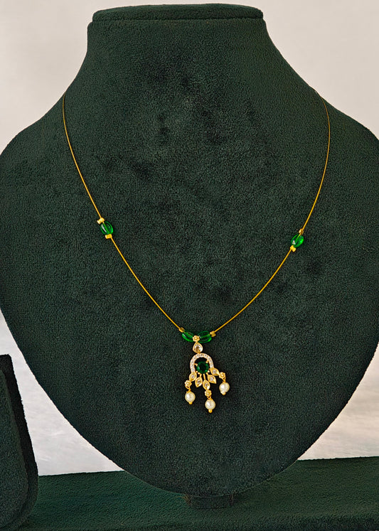 A gold chain necklace with green bead accents and a dangling pendant, displayed on a dark green velvet jewelry bust.