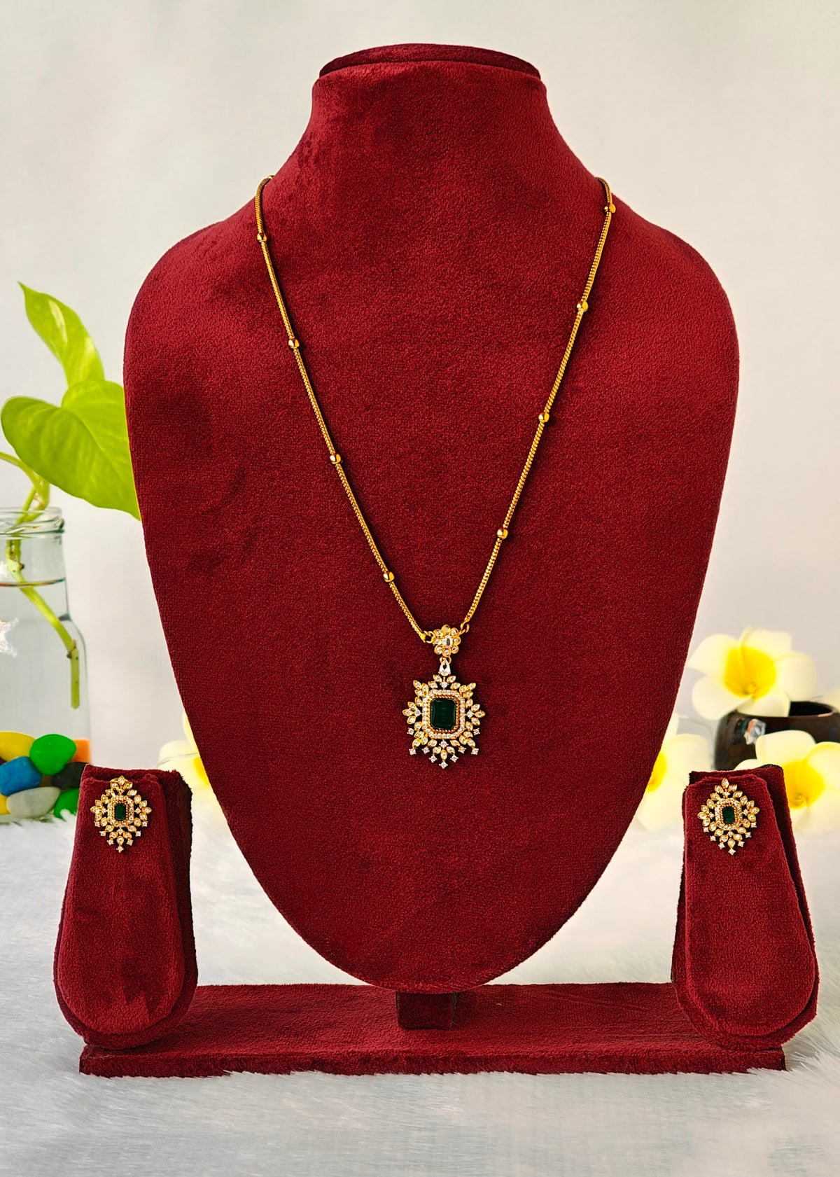 Gold necklace and matching earrings displayed on a dark red velvet jewelry bust set against a light background with decorative flowers.