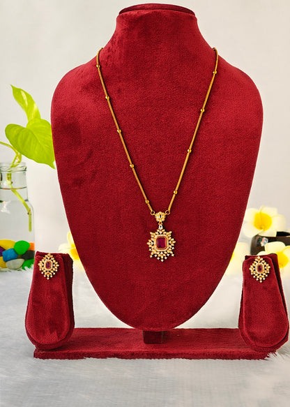Gold-toned traditional Indian jewelry set featuring a necklace with a rectangular red stone pendant, a matching bracelet, and a pair of earrings, displayed on a red velvet jewelry bust.