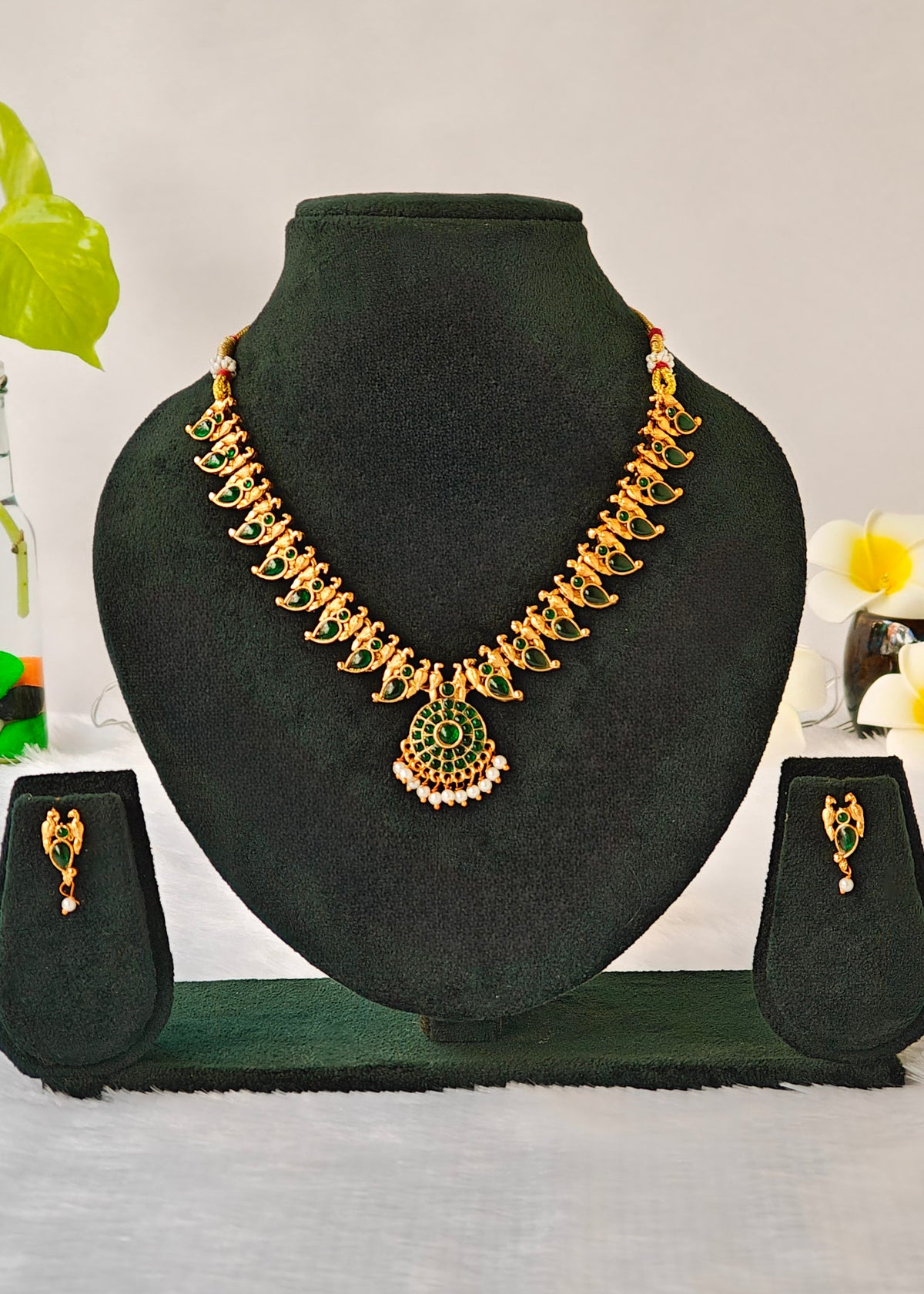 Gold and green jewelry set displayed on a black velvet mannequin bust, including a necklace with a matching pendant and two matching earrings on small display stands.