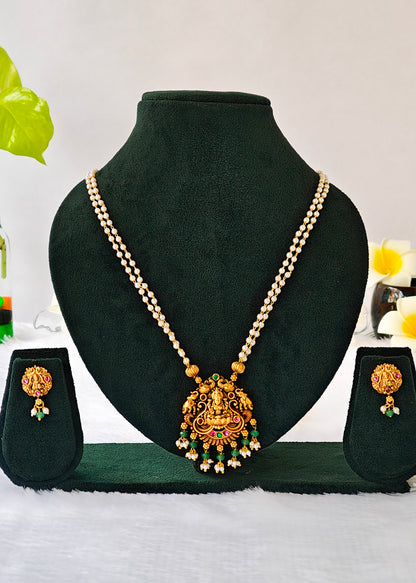 Vasudha two-strand pearl necklace with a Lakshmi and elephant pendant, green bead drops and matching earrings on a black display.
