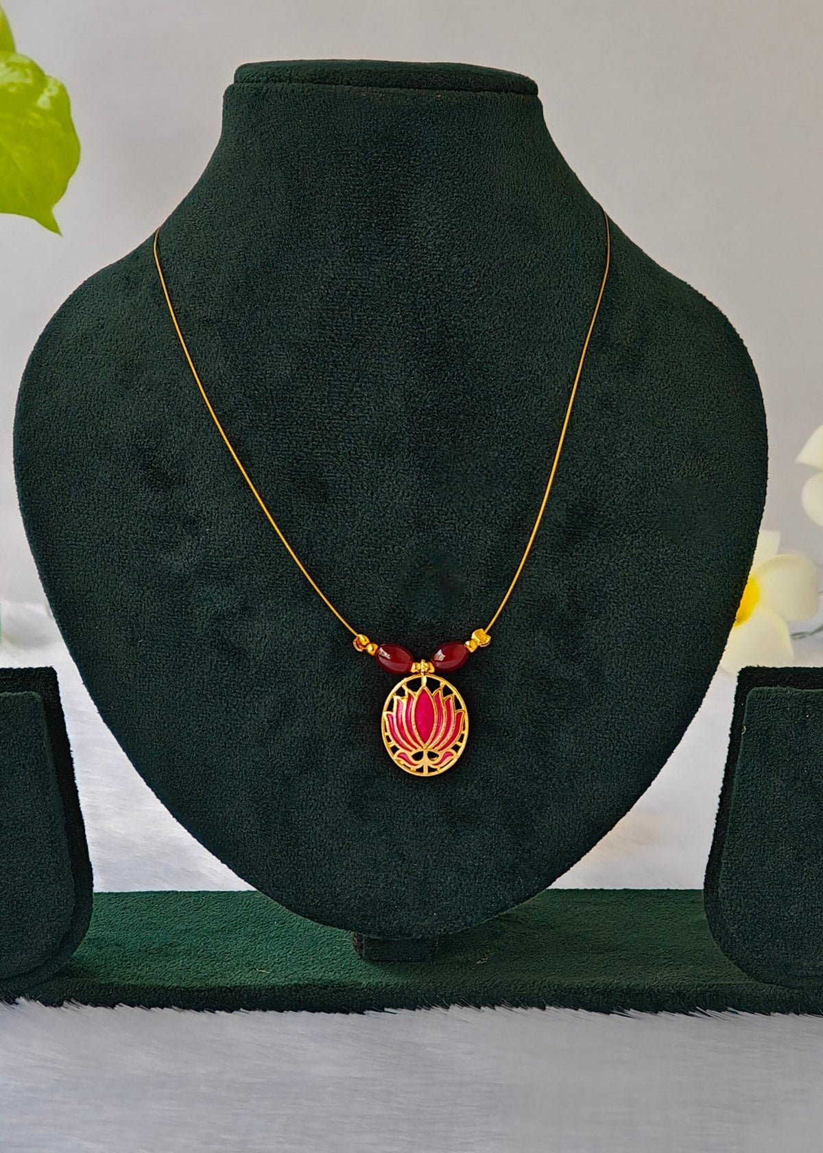 Suhani fine-wire necklace with a magenta enamel lotus pendant and dark red beads on a black display.