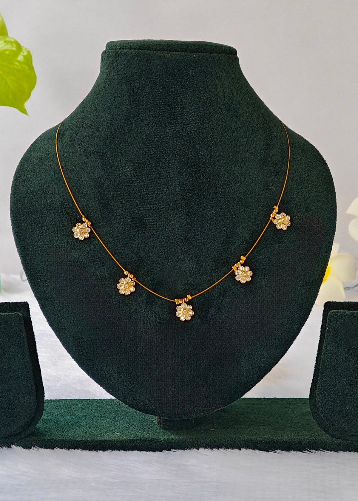 Siya fine gold-tone wire necklace with five clear crystal flower charms on a black display.