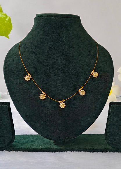 Siya fine gold-tone wire necklace with five clear crystal flower charms on a black display.