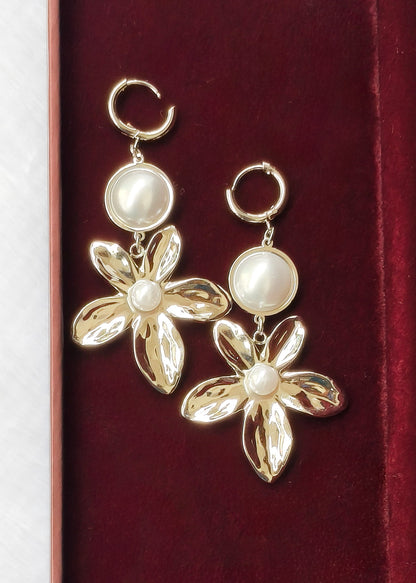 A pair of gold-tone dangle earrings with circular pearl-like beads and flower-shaped lower charms, displayed on a dark red velvet surface.