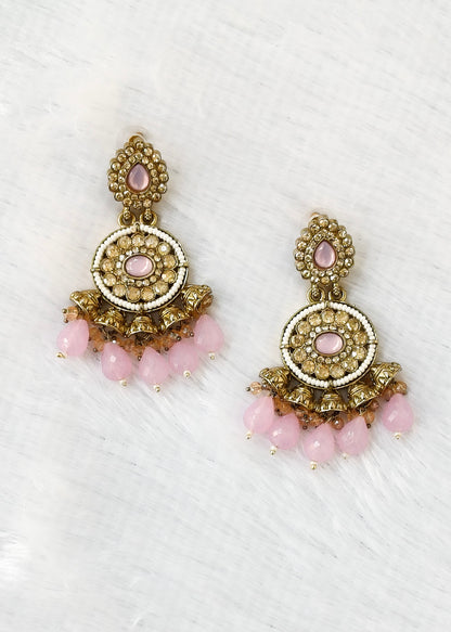 A pair of ornate gold-toned chandelier earrings with pink stones and dangling pink bead drops, displayed on a white textured background.