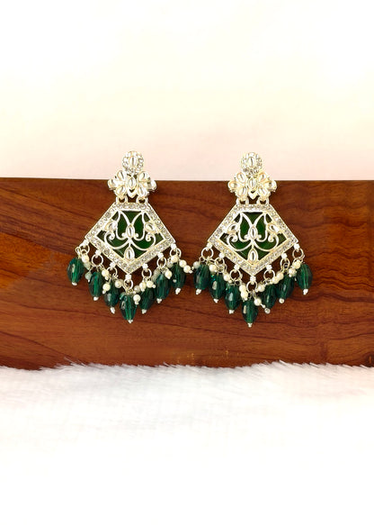 A pair of ornate gold-toned chandelier earrings with green stone inlay and dangling green bead drops, displayed on a wooden block against a white background.
