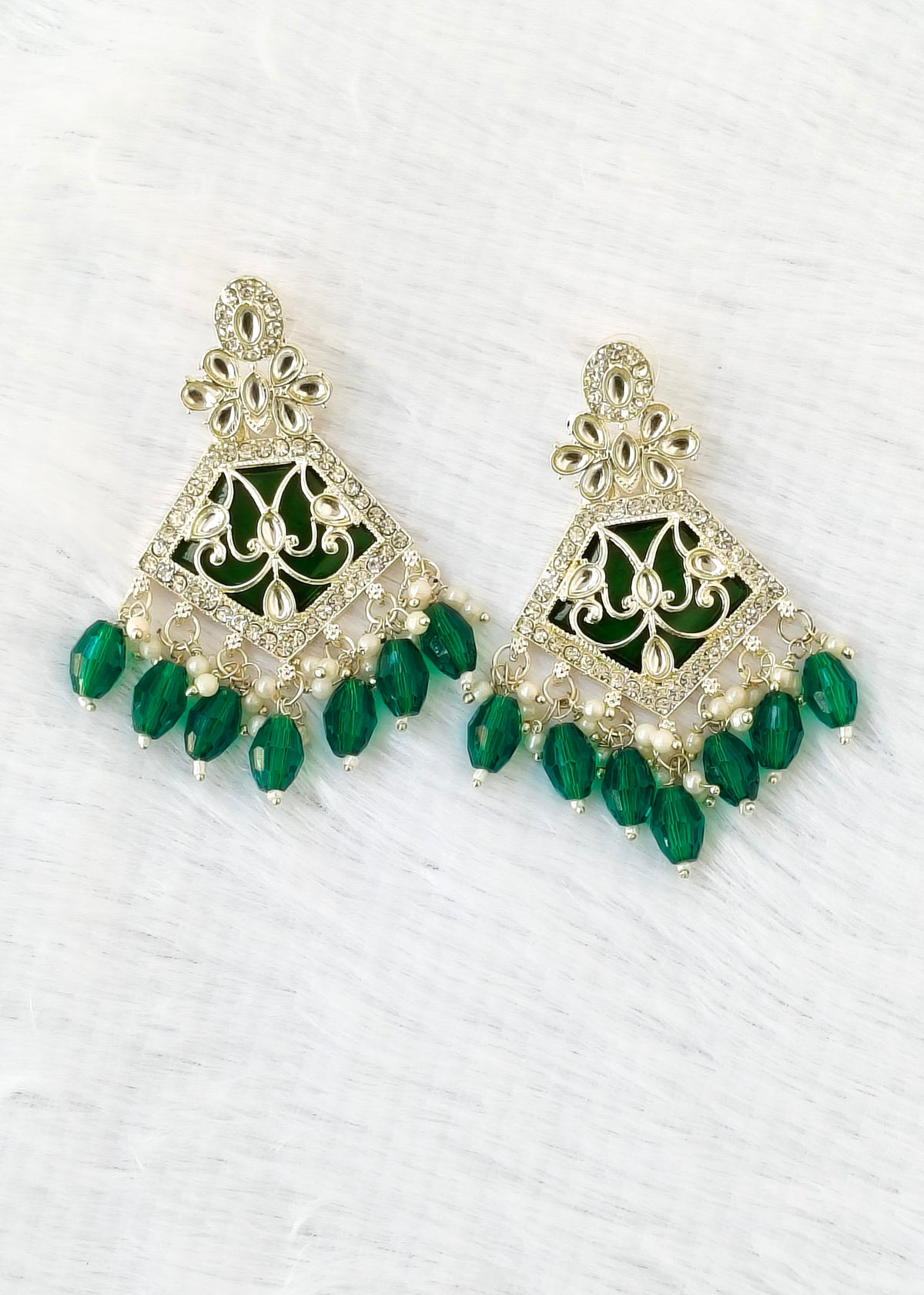 A pair of gold-plated Indian-style dangle earrings with green enamel and green faceted bead drops, displayed on a white textured background.