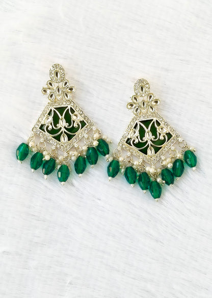 A pair of gold-plated Indian-style dangle earrings with green enamel and green faceted bead drops, displayed on a white textured background.