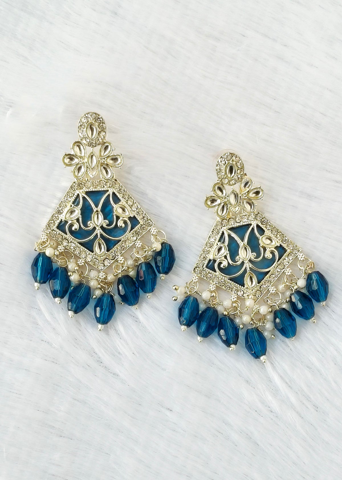 A pair of gold-plated Indian-style jhumka earrings with deep blue glass beads and small white pearl accents, displayed on a white textured background.