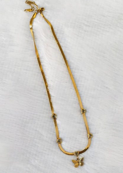 A gold snake chain necklace with a small butterfly pendant, laid flat on a white textured background.